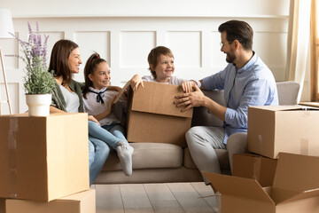 Overjoyed young Caucasian family with little kids have fun unpack unbox relocating to new home...
