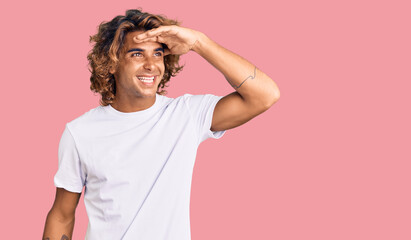 Young hispanic man wearing casual white tshirt very happy and smiling looking far away with hand...