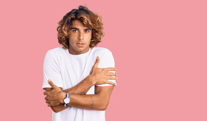 Young hispanic man wearing casual white tshirt shaking and freezing for winter cold with sad and...