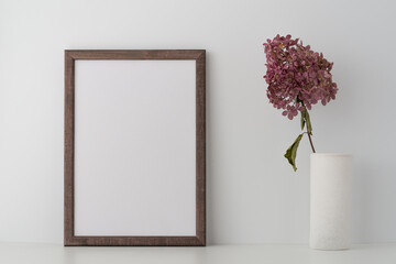 An empty wooden frame and dry decorative branch in a vase on a shelf or table, near a white wall. Whites colors. Clean, modern, minimal frame, the layout of the poster. Internal interior.