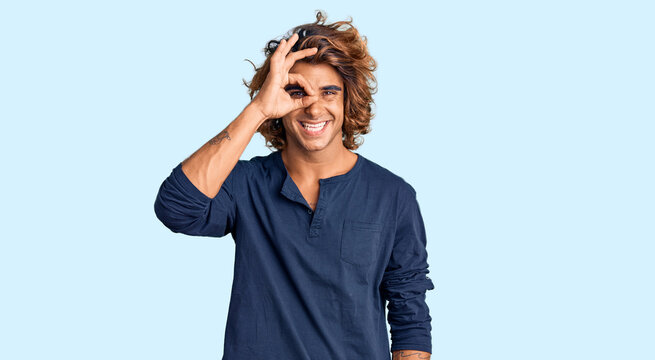 Young hispanic man wearing casual clothes doing ok gesture with hand smiling, eye looking through fingers with happy face.