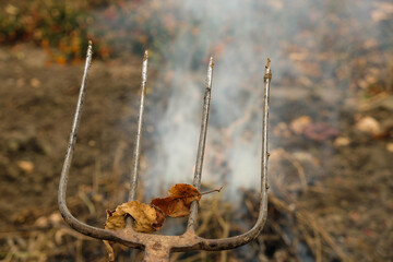 Pitchfork on a brown background of the autumn garden. Smoke from burnt herbs. Copy space.