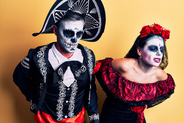 Young couple wearing mexican day of the dead costume over yellow suffering of backache, touching...