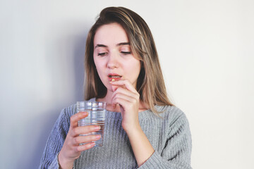 Young woman taking pill on light background, closeup