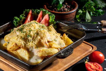 Fried potatoes with cheese and green onion on dark background