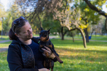 Young woman enjoys companionship with her beloved pinscher dog in a city park. Selective focus with...