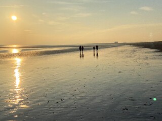 Fototapeta na wymiar beach walk at sunset people walking reflected on wet sand beach at Wichelsea beach East Sussex UK