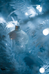 Christmas ball hanging from white christmas tree, lights and blue mood. Selective focus.