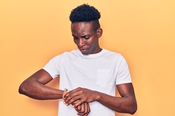 Young african american man wearing casual clothes checking the time on wrist watch, relaxed and...