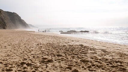 Beautiful misty golden day on a beach in Portugal with two people walking in the distance