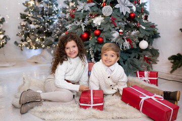 Happy little children with gift boxes in their hands near Christmas tree and light on background. Merry Christmas and Happy Holidays.