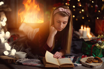 relaxing with a book - a young woman is reading a book by the fireplace