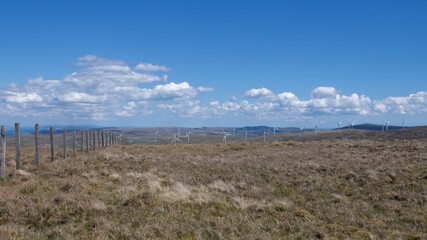Wind farm and peat land on top of Scottish hills under blue sky with little fluffy clouds