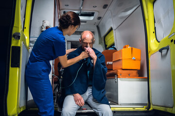 A young nurse in a uniform gives an oxygen mask to an injured man in a blanket.