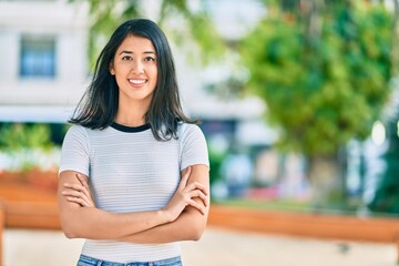 Young hispanic woman with crossed arms smiling happy at the park.