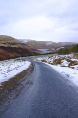 frozen road in Scottish hills covered in a little snow and a frozen dam