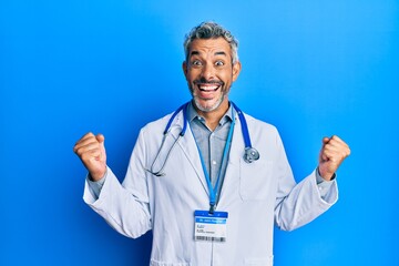 Middle age grey-haired man wearing doctor uniform and stethoscope celebrating surprised and amazed for success with arms raised and open eyes. winner concept.