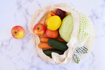 Eco friendly mesh bag with green fresh vegetable and fruits on the marbel background.