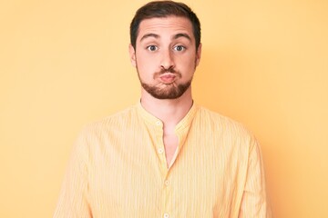 Young handsome man wearing casual clothes puffing cheeks with funny face. mouth inflated with air,...