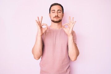 Naklejka premium Young handsome man wearing casual tshirt relax and smiling with eyes closed doing meditation gesture with fingers. yoga concept.