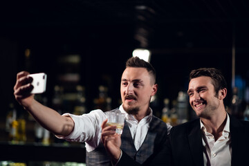 two friends meet in a bar and take a selfie on their smartphone.