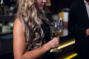 blonde girl in a black dress holding a glass of champagne close up.