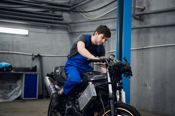 Mechanic sitting on a motorcycle with a tool in his hand