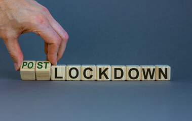 Symbol for a post-lockdown time. Male hand turns cubes and changes the word 'lockdown' to 'postlockdown'. Beautiful grey background. Medical and covid-19 pandemic concept, copy space.