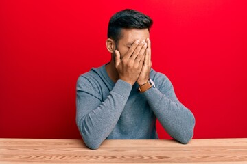 Obraz premium Handsome hispanic man wearing casual style sitting on the table with sad expression covering face with hands while crying. depression concept.