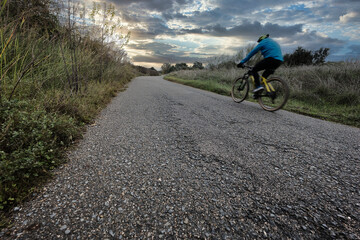 Obraz premium Cyclist with mountain bike on poorly paved rural road and with sky about to rain