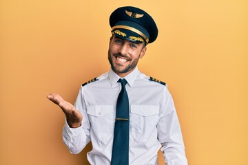 Handsome hispanic man wearing airplane pilot uniform smiling cheerful with open arms as friendly welcome, positive and confident greetings