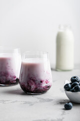 two glasses of blueberry milkshake on a light background