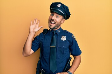Handsome hispanic man wearing police uniform waiving saying hello happy and smiling, friendly welcome gesture © Krakenimages.com