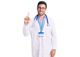 Fototapeta na wymiar Young hispanic man wearing doctor uniform and stethoscope showing and pointing up with finger number one while smiling confident and happy.