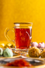 Tea with saffron, white glass cup, silver spoon, dates with chocolate on a golden background
