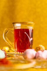 Tea with saffron, white glass cup, silver spoon, dates with chocolate on a golden background