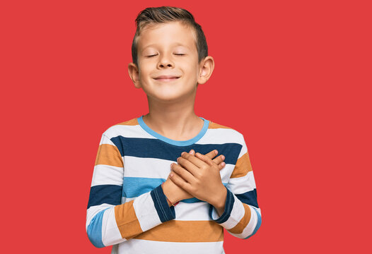 Adorable caucasian kid wearing casual clothes smiling with hands on chest with closed eyes and grateful gesture on face. health concept.