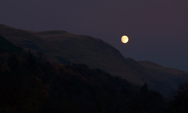 full moon rising above Scottish hills to a clear purple tinted sky