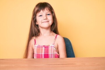 Little caucasian kid girl with long hair wearing casual clothes sitting on the table with a happy and cool smile on face. lucky person.