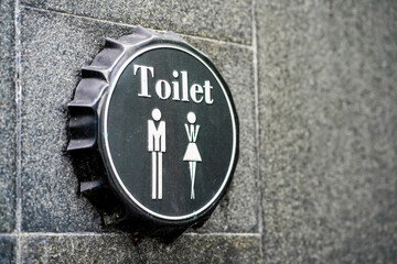 A toilet sign on a black beer bottle cap attached on cement wall texture with copy space