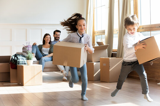 Happy little kids have fun carry unpack boxes moving in to new home with parents. Excited children unbox packages celebrate relocation to own house. Family relocation, real estate, rental concept.