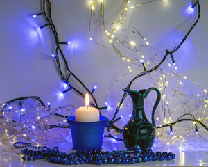 blue composition with candle and miniature mug, blue pearl ornaments in the foreground, white and...