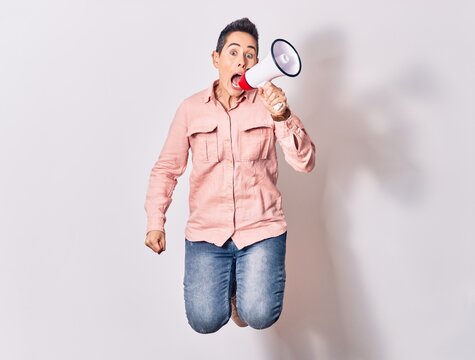 Young beautiful caucasian woman screaming using megaphone. Jumping over isolated white background