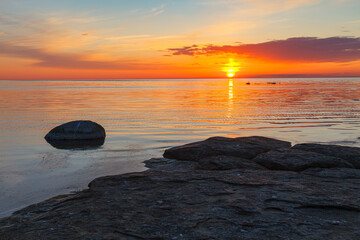Fototapeta na wymiar Beautiful colorfull sunset over the sea shore with rocks under shallow water