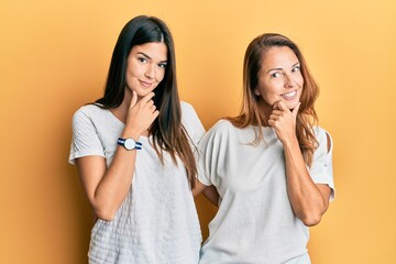 Hispanic family of mother and daughter wearing casual white tshirt looking confident at the camera smiling with crossed arms and hand raised on chin. thinking positive.