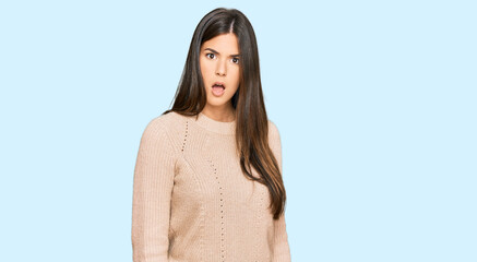 Young brunette woman wearing casual winter sweater in shock face, looking skeptical and sarcastic,...