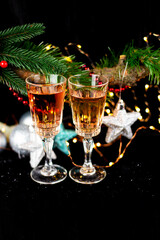 New Year and Christmas decor. Glasses for champagne, toys for the Christmas tree stand on the table in front in the dark, beautiful bokeh on the background.