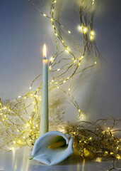 white burning candle, beautiful and noble white callas flower, illuminated background of a chain of...