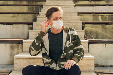 Young handsome man wearing a white medical mask poses while straightening his mask. Images of the man wearing a mask due to the pandemic from various angles.