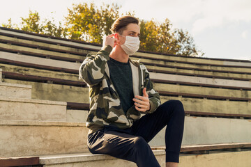Obraz premium Young handsome man wearing a white medical mask poses while straightening his mask. Images of the man wearing a mask due to the pandemic from various angles.
